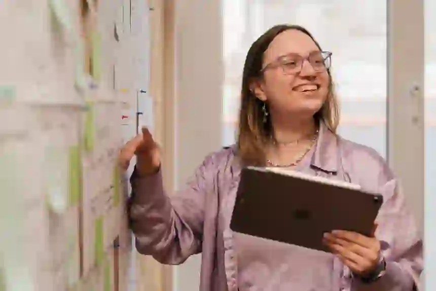 Our web devloper, Awen holding an ipad and pointing towards some sticky notes on a wall.